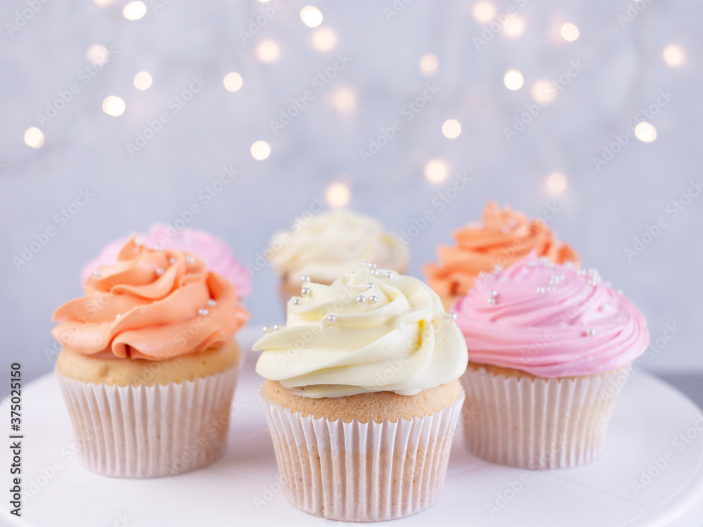 Cupcakes with color cream on blurred lights background with copy space. Birthday celebration concept.