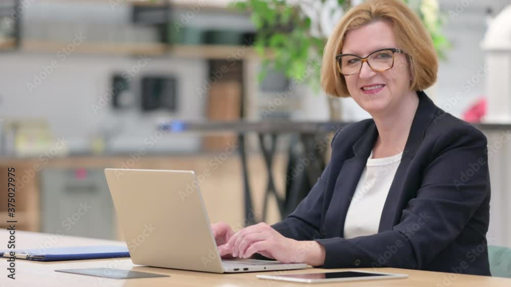 Old Businesswoman with Laptop Smiling at Camera in Office Old Businesswoman with Laptop Smiling at Camera in Office