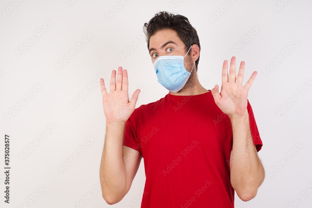 Young caucasian man with short hair wearing medical mask standing over isolated white wall Moving away hands palms showing refusal and denial with afraid and disgusting expression. Stop and forbidden. Young caucasian man with short hair wearing medical mask standing over isolated white wall Moving away hands palms showing refusal and denial with afraid and disgusting expression. Stop and forbidden.