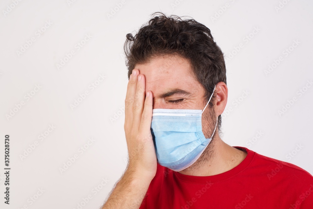 Young caucasian man with short hair wearing medical mask standing over isolated white background Yawning tired covering half face, eye and mouth with hand. Face hurts in pain. Young caucasian man with short hair wearing medical mask standing over isolated white background Yawning tired covering half face, eye and mouth with hand. Face hurts in pain.