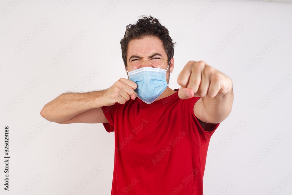 Portrait of strong and determined Young caucasian man with short hair wearing medical mask standing over isola punching air with fist and looking confidently at camera, male struggle, fighting spirit. Portrait of strong and determined Young caucasian man with short hair wearing medical mask standing over isola punching air with fist and looking confidently at camera, male struggle, fighting spirit.