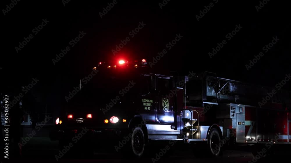 Firetruck with flashing lights in the dark night. Firemen and local people walking around the vehicle and entering a driver's seat. Fire department truck illuminated by flashing emergency lights. Firetruck with flashing lights in the dark night. Firemen and local people walking around the vehicle and entering a driver's seat. Fire department truck illuminated by flashing emergency lights.