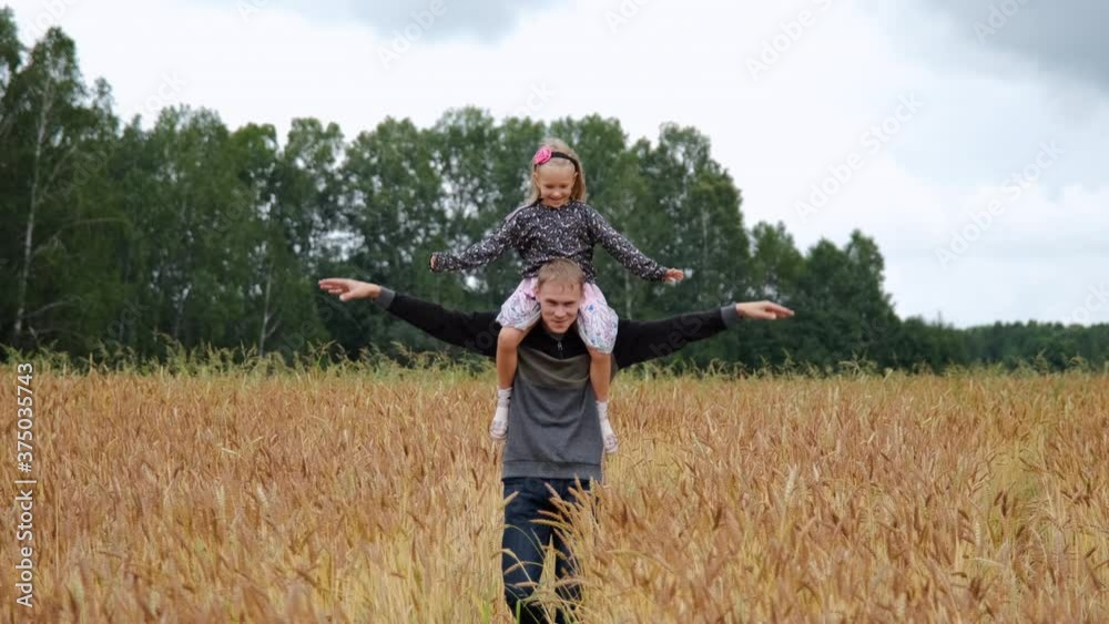 Dad Giving Daughter Piggyback Ride in a Wheat Field. Child Flying on Father Shoulders. Concept of Fathers Day, Freedom, Harmony with Nature and Summer Vacation Dad Giving Daughter Piggyback Ride in a Wheat Field. Child Flying on Father Shoulders. Concept of Fathers Day, Freedom, Harmony with Nature and Summer Vacation