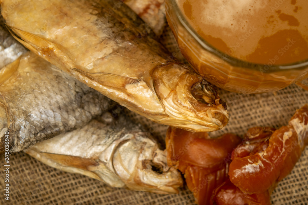 Dried fish, dried caviar and a beer mug on a homespun cloth with a rough texture. Close up.