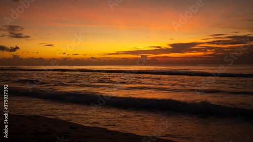 Seascape. Beach at sunset during high tide. Sunset golden hour. Sun at horizon line. Bright sunlight reflection in water. Balangan beach, Bali, Indonesia