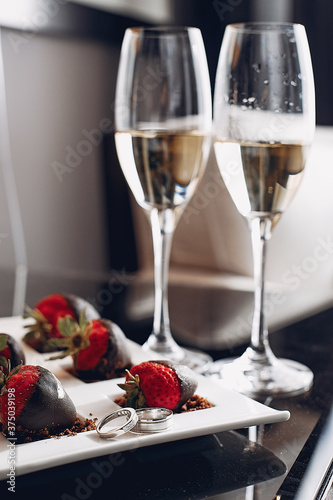 Elegant wedding rings on a plate. Champagne with starawberry on a chocolate photo