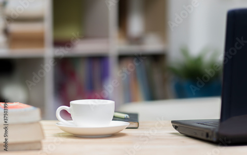 Office desk with a cup of coffee and laptop with book shelf background