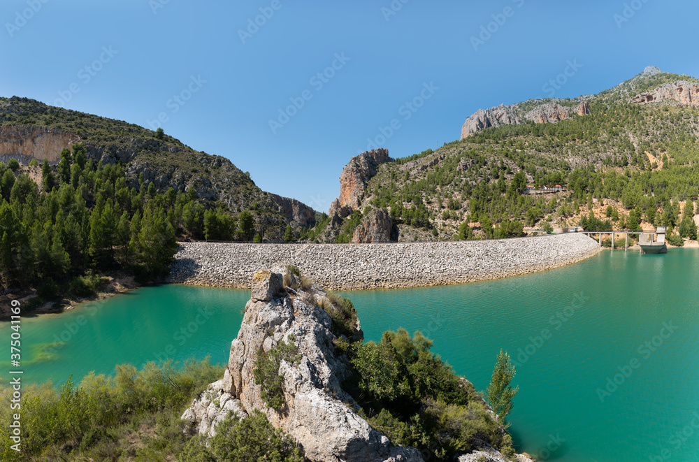 Summer with blue sky in Castilles in Spain. View of the dam of Lake Taibilla with an imposing rock in the foreground. The pump station is on the right.