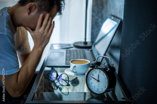 headache, tense young asian man working on laptop computer in bedroom at night photo