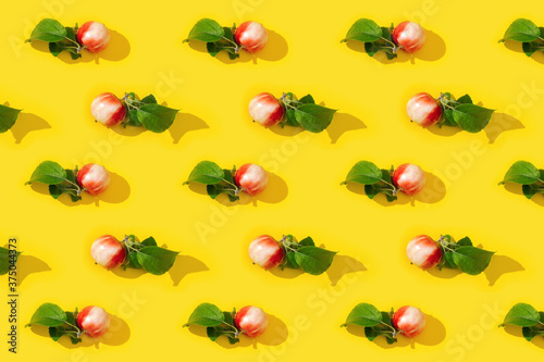 Regular creative pattern from ripe small red apples and green leaves  food concept.