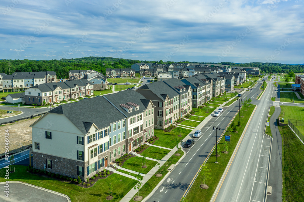 Aerial view of a new neighborhood street lined with modern townhouses with colorful facade in the East Coast United States dreamy cloudy blue sky
