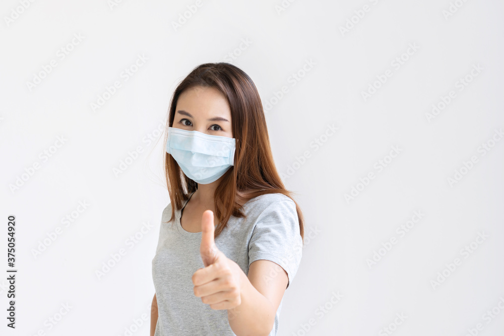 Portrait of cheerful young Asian girl with protective face mask thumb up posing and smiling at camera over white background. Copy space Portrait of cheerful young Asian girl with protective face mask thumb up posing and smiling at camera over white background. Copy space