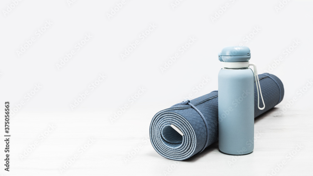 Rolled blue yoga mat and blue water bottle on grey wooden surface