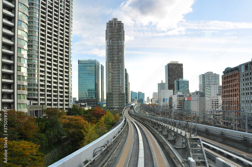 Riding on monorail train to Odaiba Island among modern and Futuristic architecture of Tokyo city and autumn color trees