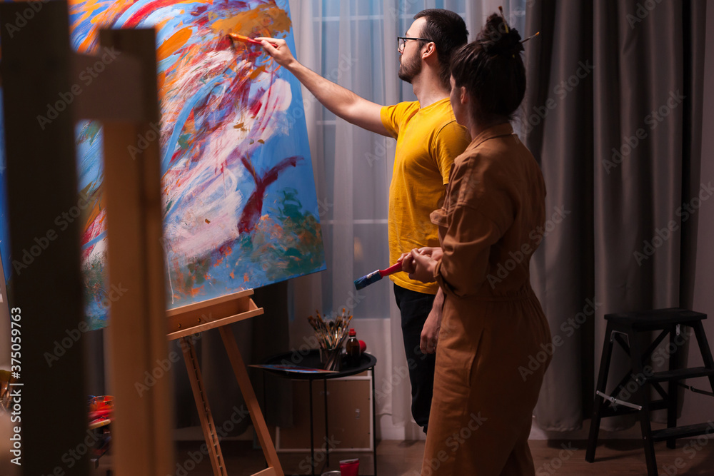 © DC Studio - Young man learning to paint on canvas from successful painter. Modern artwork paint on canvas, creative, contemporary and successful fine art artist drawing masterpiece