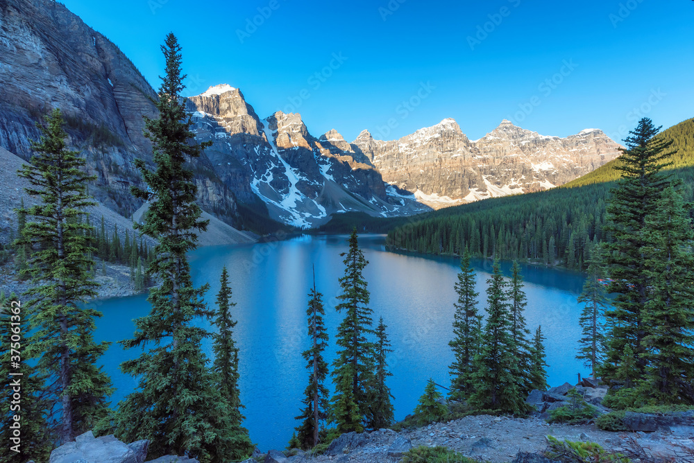 Beautiful turquoise waters of the Moraine Lake at sunrise with snow-covered peaks above it in Rocky Mountains, Banff National Park, Canada.	