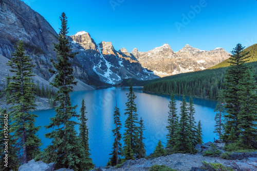 Beautiful turquoise waters of the Moraine Lake at sunrise with snow-covered peaks above it in Rocky Mountains, Banff National Park, Canada. 