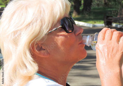  blonde woman in sunglasses drinks water from a bottle quenches thirst 