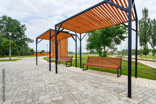 The two wooden benches with the canopies covering them from sunlight on the walkway in a new city park