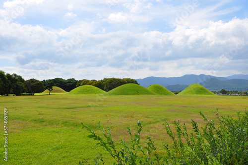 Tumuli, a mound of earth and stones, among green grass field in Gyeongju, the capital of the ancient kingdom of Silla