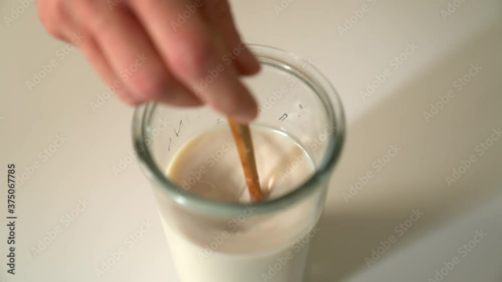 Closeup hand mixing the liquid of floor and milk with a wooden spoon in a glass. Dough making, bakery and cooking concept