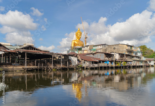 The Giant Golden Buddha in Wat Paknam Phasi Charoen Temple in Phasi Charoen district with boat on Chao Phraya River at noon, Bangkok urban city, Thailand. photo