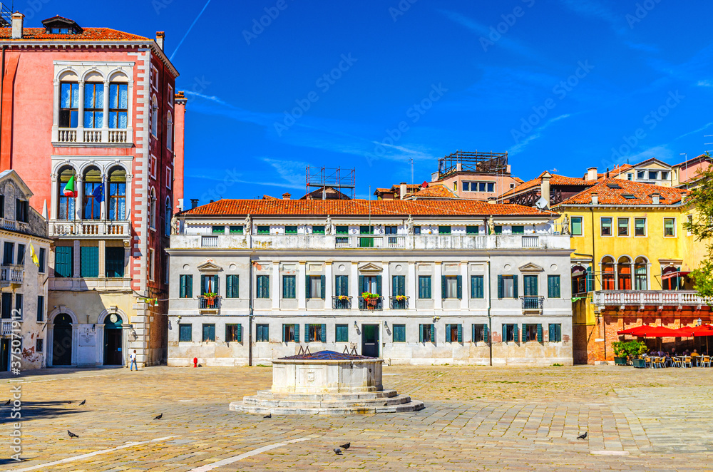Palace buildings and stone well on Campo San Polo square in Venice historical city centre, blue sky background in summer day, Veneto Region, Northern Italy