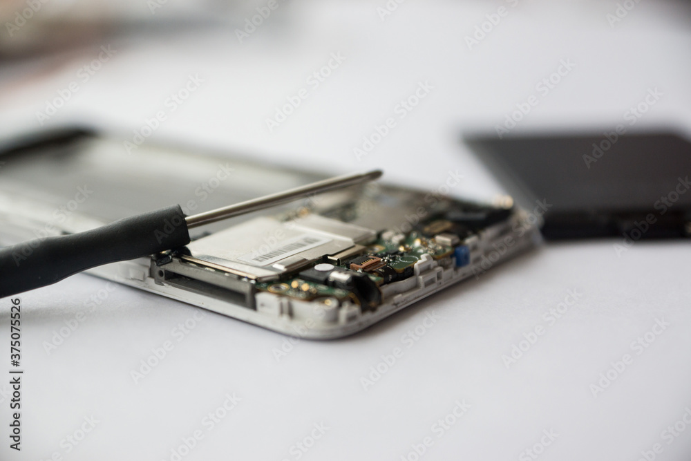 A screwdriver on a disassembled phone. Repair of smartphones, replacement of malfunctions in the gadget. Macro. Selective focus, shallow depth of field A screwdriver on a disassembled phone. Repair of smartphones, replacement of malfunctions in the gadget. Macro. Selective focus, shallow depth of field