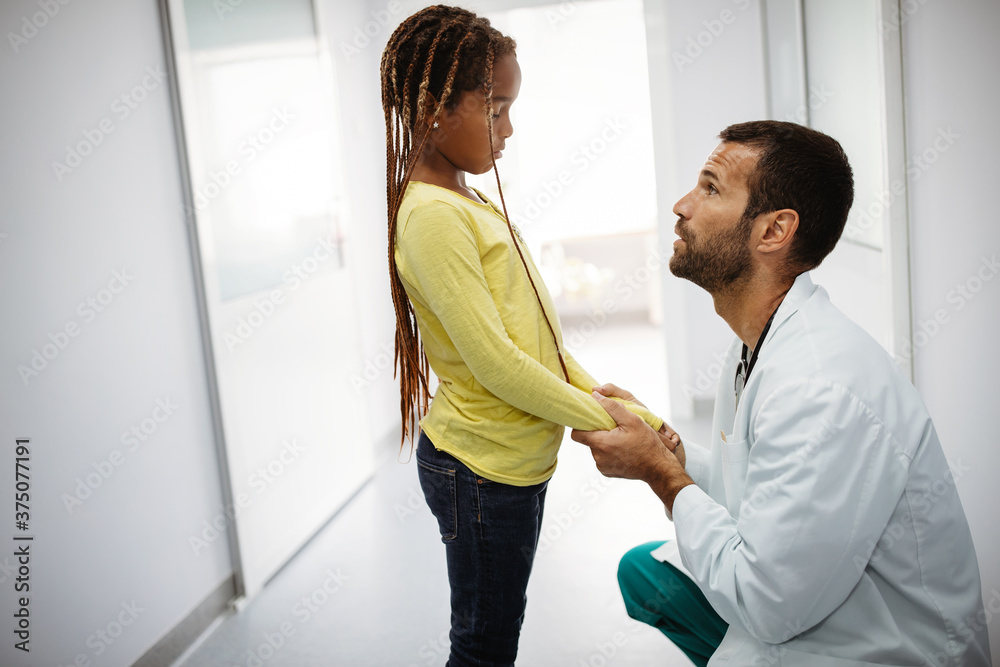 Doctor comforting, supporting a worried sad girl kid in hospital