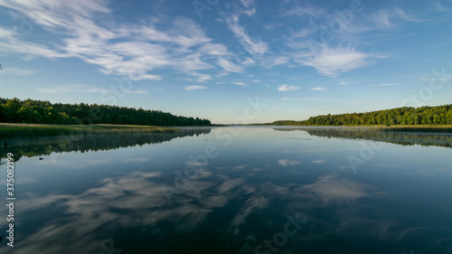 cloud reflections in clear and calm lake water  forest in the background  summer morning
