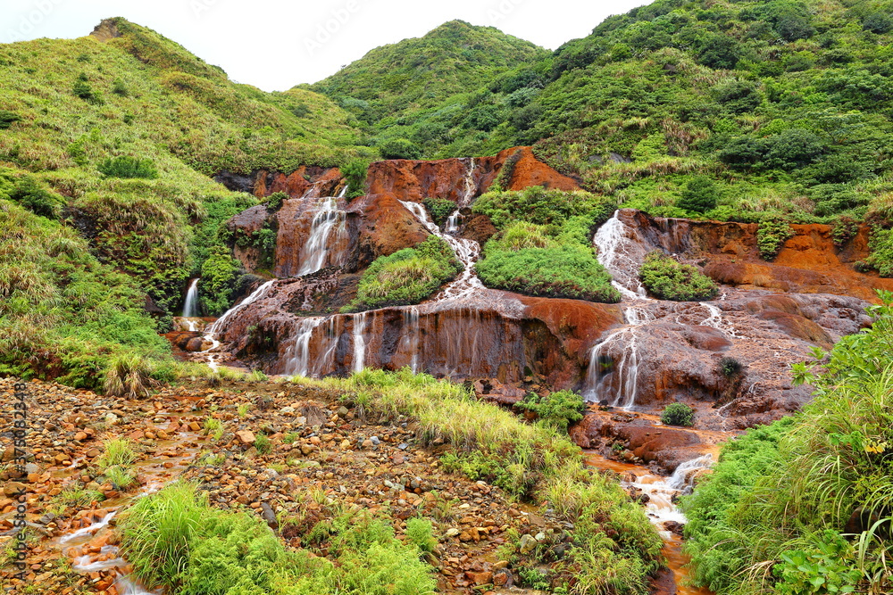Obraz premium Golden Waterfall flowing over rust-colored rocks & soil due to minerals from a former mining area in Taipei, Taiwan