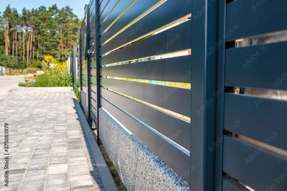 Modern panel fencing in anthracite color, visible spans and a wicket, forest in the background. Modern panel fencing in anthracite color, visible spans and a wicket, forest in the background.