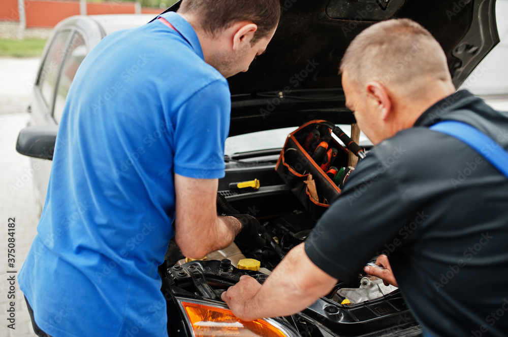 Car repair and maintenance theme. Two mechanics in uniform working in auto service, checking engine. Car repair and maintenance theme. Two mechanics in uniform working in auto service, checking engine.