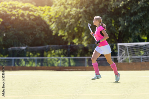 Young girl field hockey player running on pitch