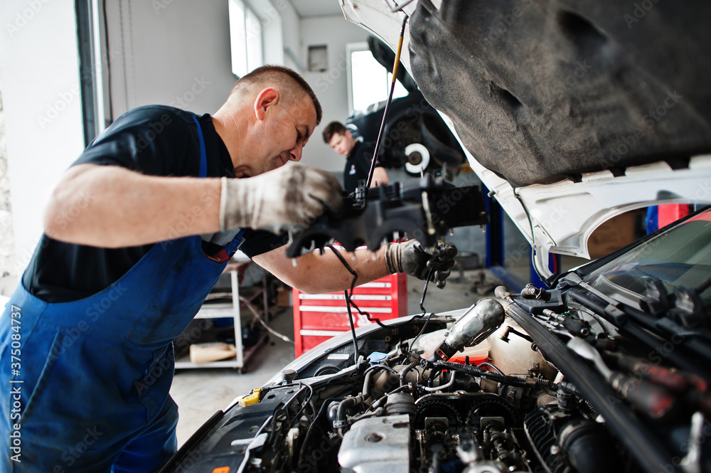 Car repair and maintenance theme. Mechanic in uniform working in auto service, checking engine. Car repair and maintenance theme. Mechanic in uniform working in auto service, checking engine.