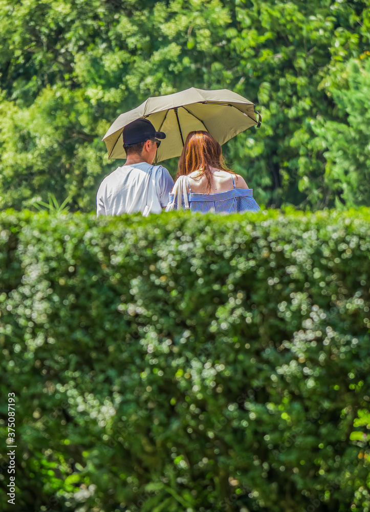 Young couple walking in the park and having an umbrella to protect from the bright sun.