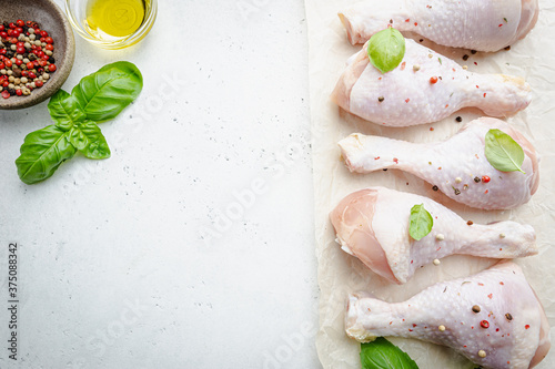 Raw chicken drumsticks on paper with herbs and seasonings on white background. Top view with copy space for your text.