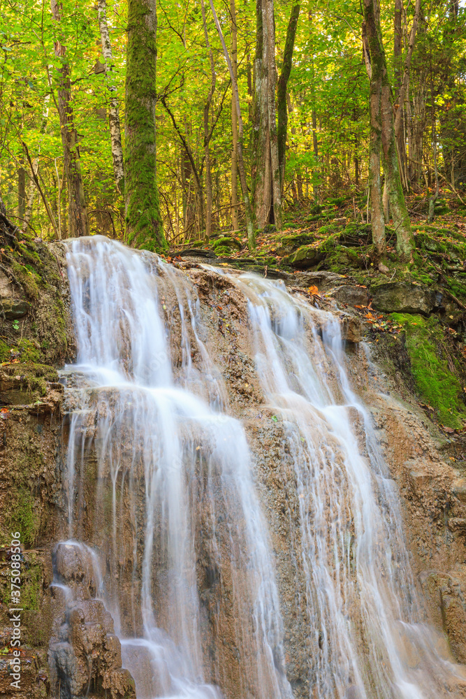 Fototapeta premium Beautiful waterfall in a deciduous forest in the autumn