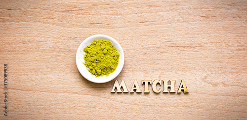 Japanese Green powder matcha tea on a platter, on a brown background. Inscription of the wooden letters in English. Loose powder. Space for text. Cooking, an ingredient for an invigorating drink