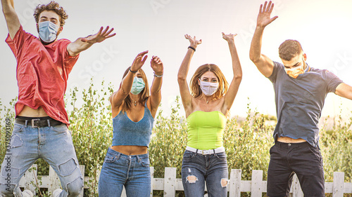 Covid-19 young people lifestyle. Friends jumping free wearing protective masks against coronavirus. New life concept