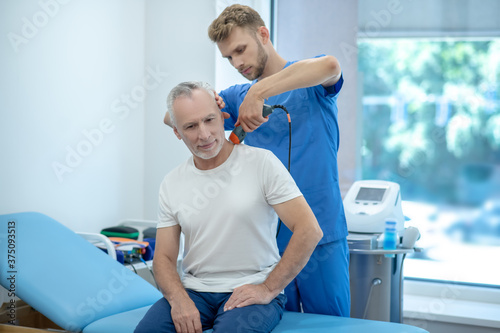 Mature patient sitting on coach  receiving ultrasound treatment of his neck