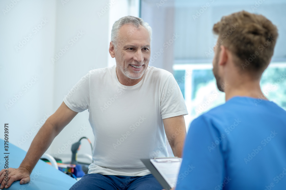 Back view of brown-haired doctor talking with mature male patient Back view of brown-haired doctor talking with mature male patient