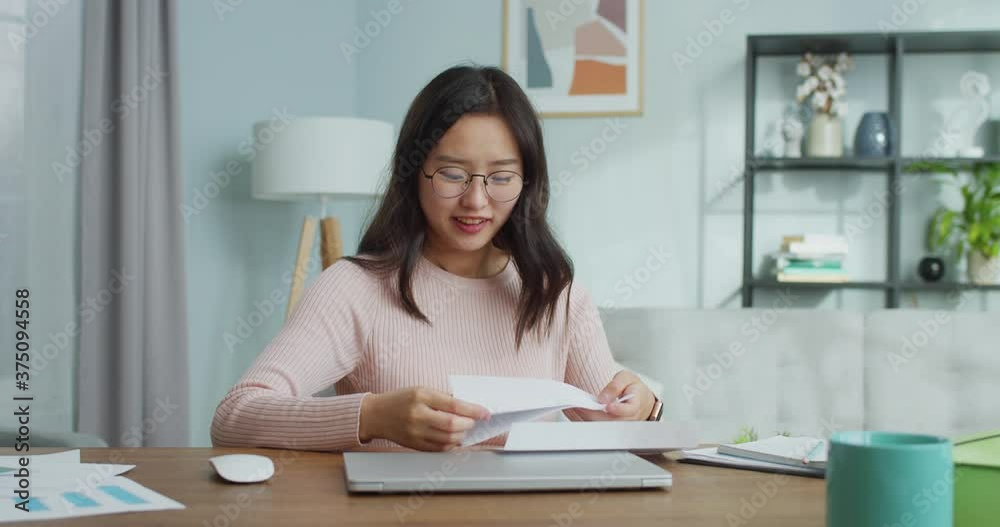 Pretty Asian woman has recieved response from university, college. Excited young girl in glasses is sitting at table and opening letter. Emotional student being sad of refusal and taling off glasses. Pretty Asian woman has recieved response from university, college. Excited young girl in glasses is sitting at table and opening letter. Emotional student being sad of refusal and taling off glasses.