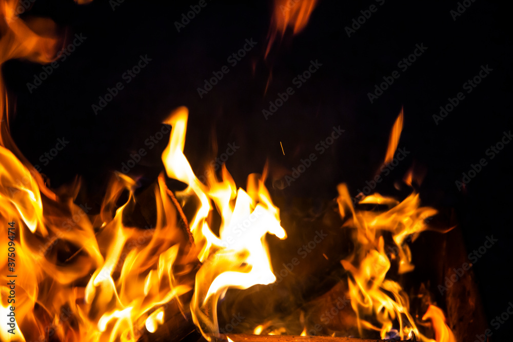 Fire on a dark background. Fire from firewood close up. Flaming burning sparks close-up, fire patterns. Red and orange Infernal glow of fire in the dark.
