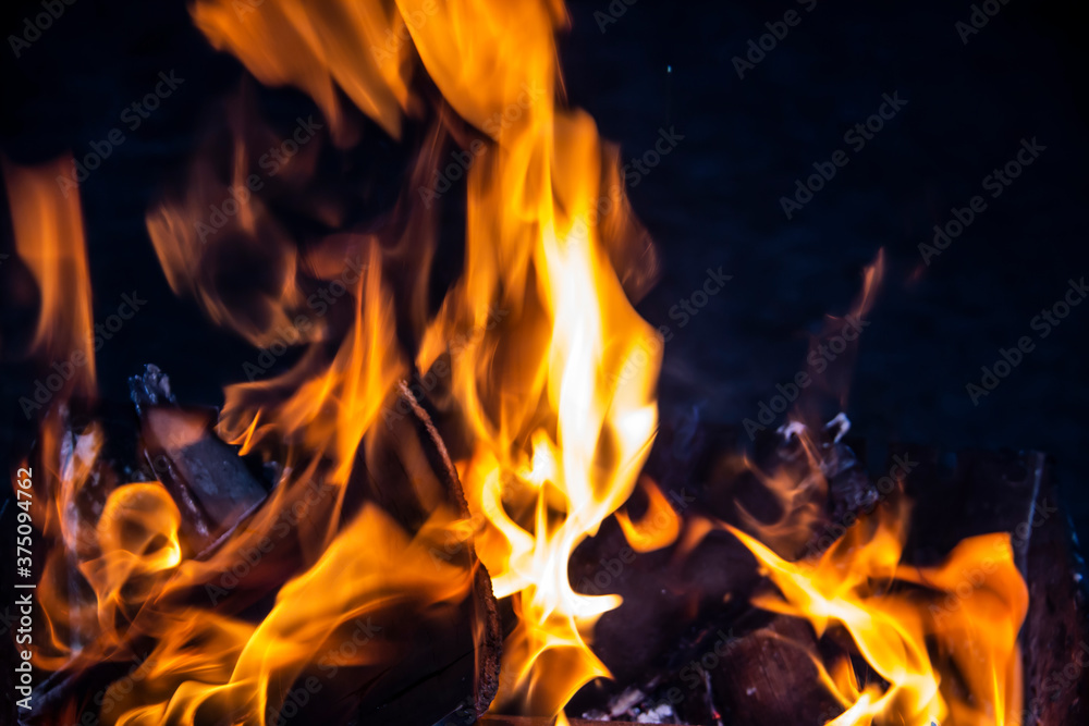 Fire on a dark background. Fire from firewood close up. Flaming burning sparks close-up, fire patterns. Red and orange Infernal glow of fire in the dark. Fire on a dark background. Fire from firewood close up. Flaming burning sparks close-up, fire patterns. Red and orange Infernal glow of fire in the dark.