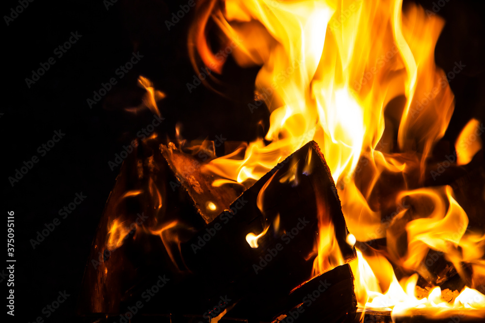 Fire on a dark background. Fire from firewood close up. Flaming burning sparks close-up, fire patterns. Red and orange Infernal glow of fire in the dark. Fire on a dark background. Fire from firewood close up. Flaming burning sparks close-up, fire patterns. Red and orange Infernal glow of fire in the dark.