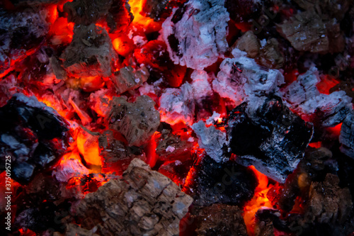 Burning coals. Close-up of decaying charcoal, barbeque season. Bright flashes of fiery flames. Burning hot coals and wood in the night. Red coals burned in the bonfire.