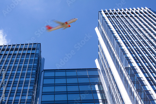 Unidentified passenger airplane flying in blue sky high above skyscrapers in perspective.