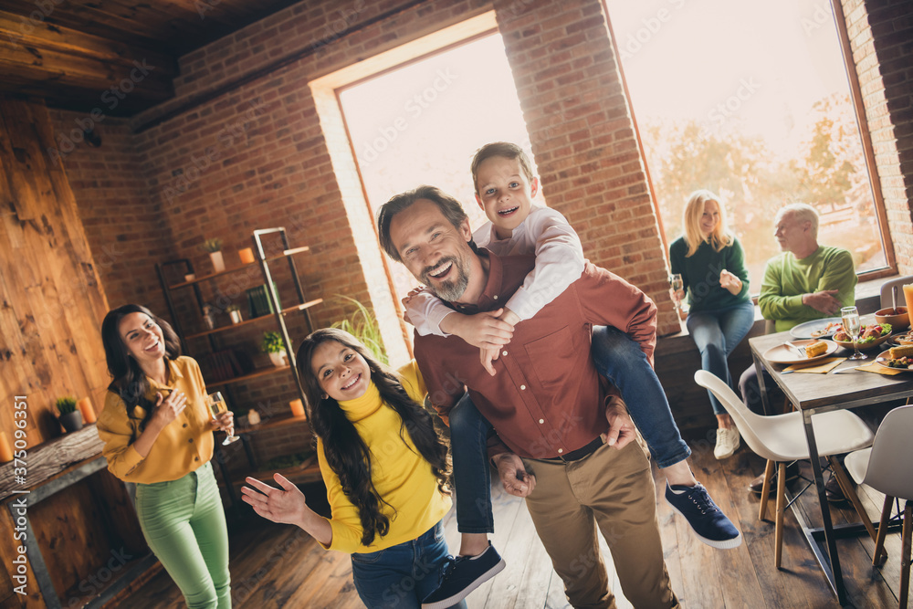 Photo of full family gathering six people two small kids play dad piggyback daughter wave hand mom laugh grandparents sit sofa dinner table generation in home evening living room indoors - obrazy, fototapety, plakaty 
