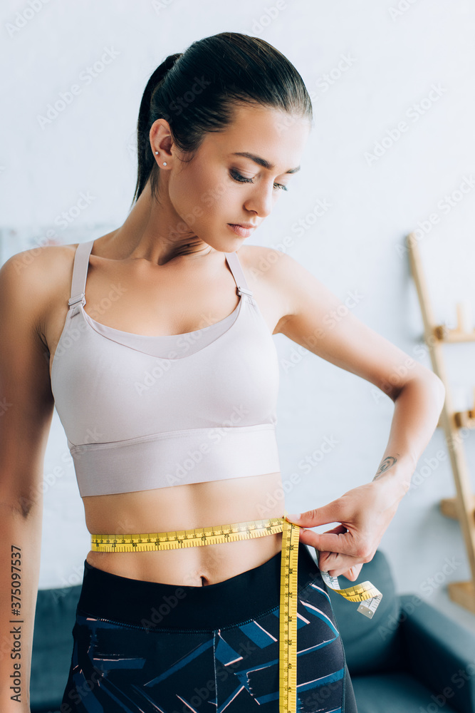 Φωτογραφία Brunette sportswoman measuring waist with tape in living room